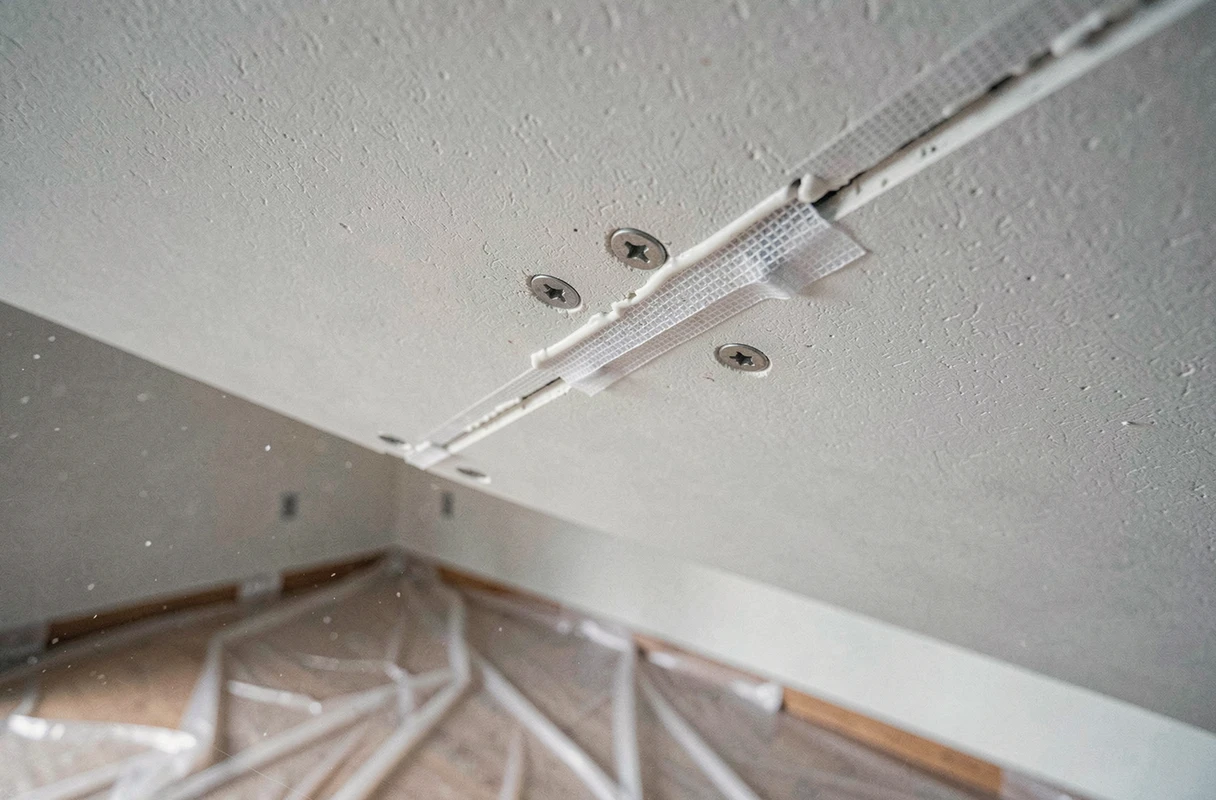 Détail de jonction entre deux plaques de plâtre BA13 avec vis et enduit de jointoiement sur un plafond en cours de finition
