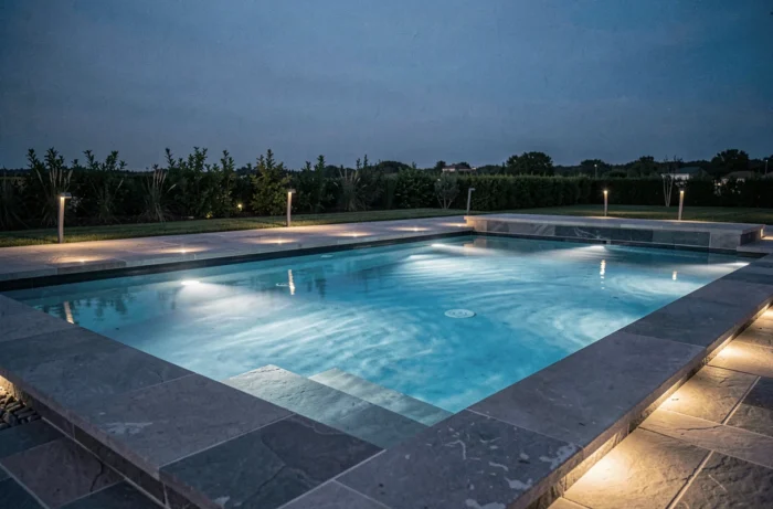 Éclairage LED encastré basse tension dans les parois et les marches d'une piscine extérieure moderne au crépuscule, reflets sur la terrasse en pierre