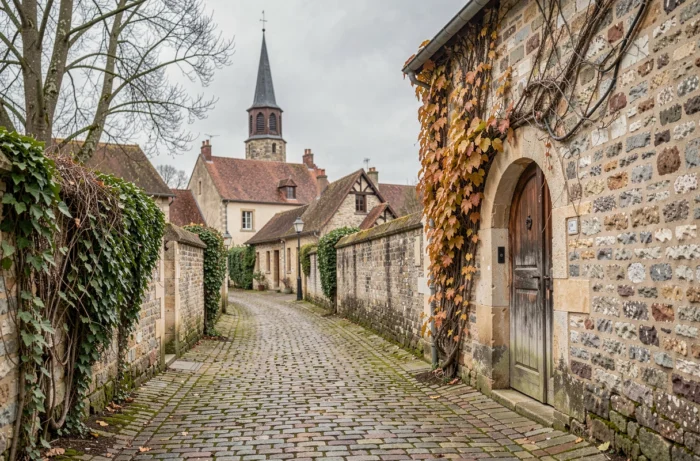 Ruelle pavée d'un village bourguignon menant à une demeure ancienne en pierre, typique de l'architecture de la région natale de Florent Pagny